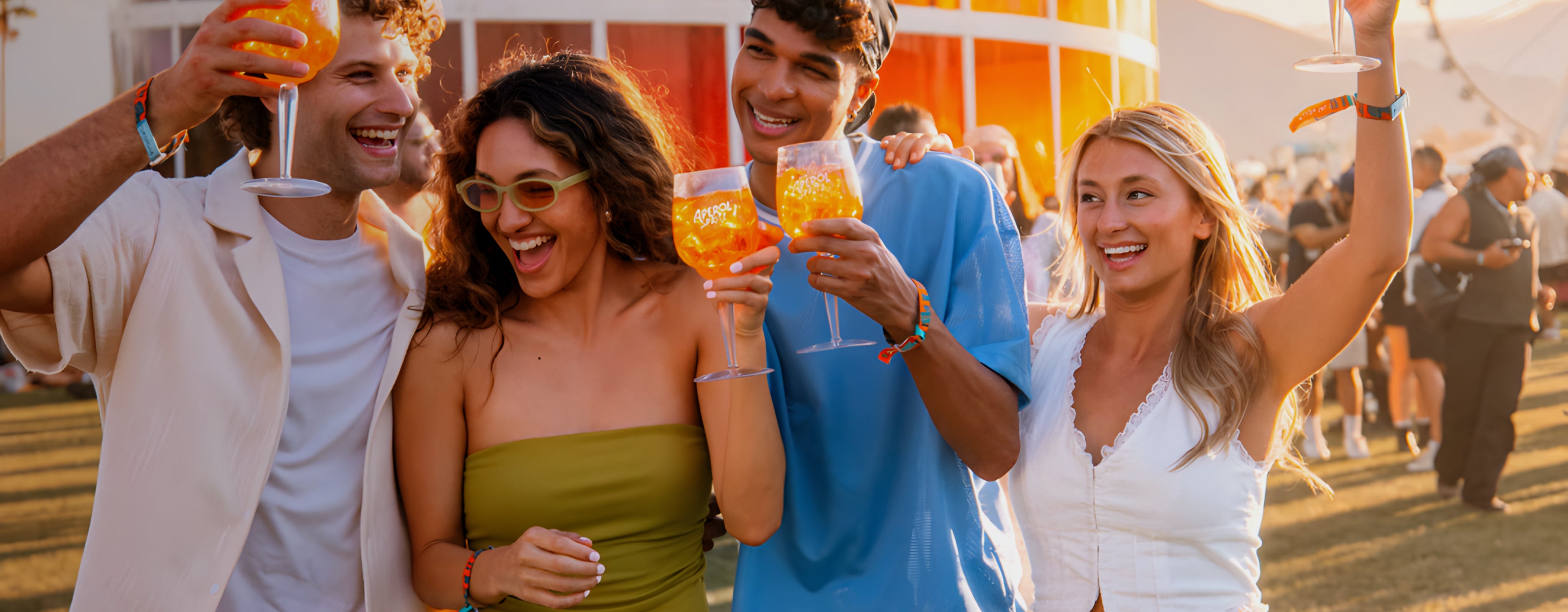 Four young adults celebrating with Aperol Spritz at an outdoor festival, smiling under the warm sunset light